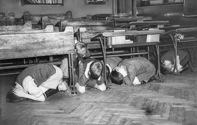 Children practicing taking cover during an Air Raid Drill while in school.