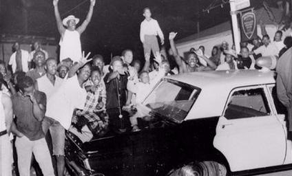 African American rioters surround a police car (1965)